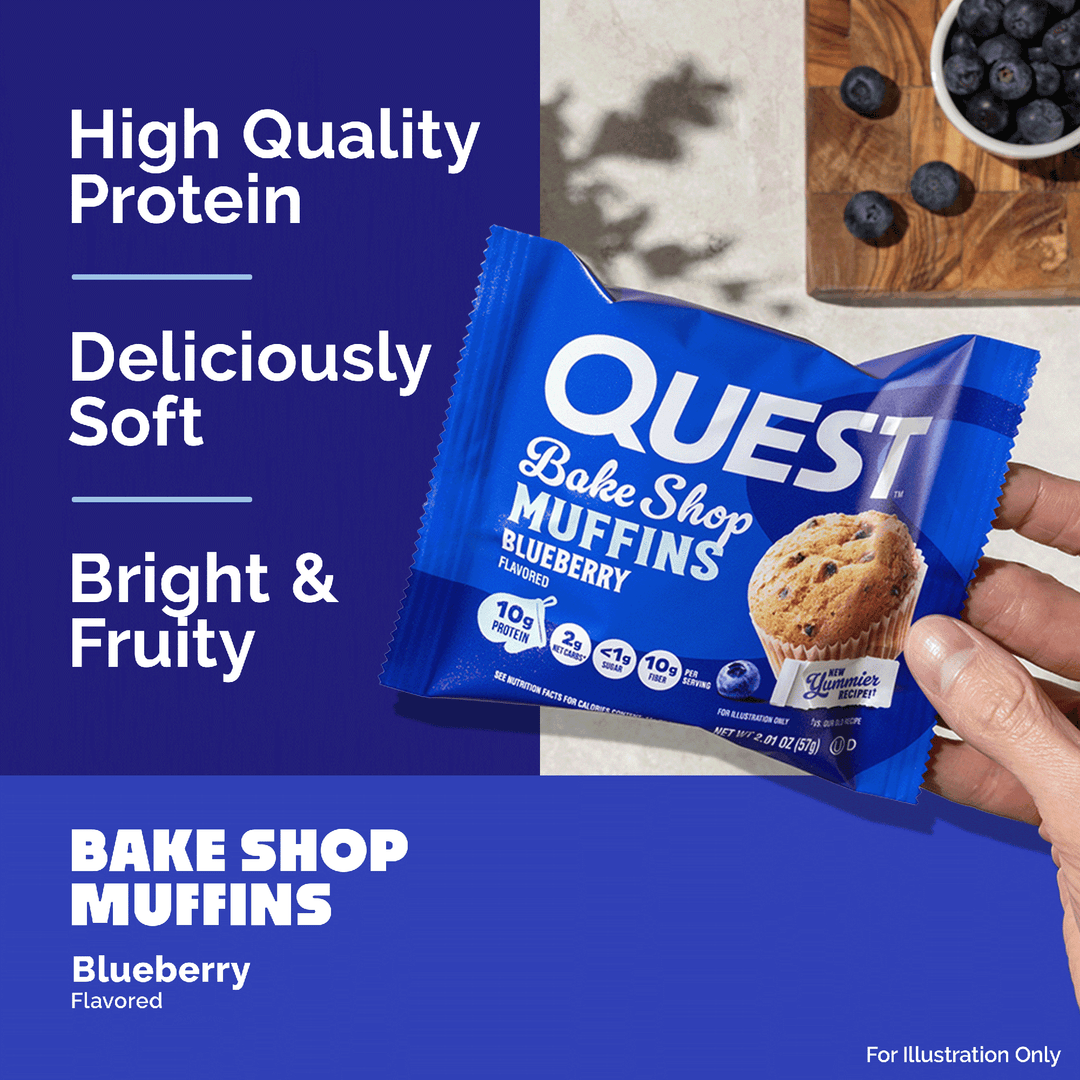 A hand holding a blue packet of QUEST Bake Shop Muffins Blueberry Flavored, set against a split background with dark blue text panels and a light beige surface showing blueberries.