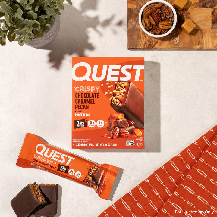 Quest Crispy Chocolate Caramel Pecan protein bar packaging on a light surface with a plant and cutting board in the background.