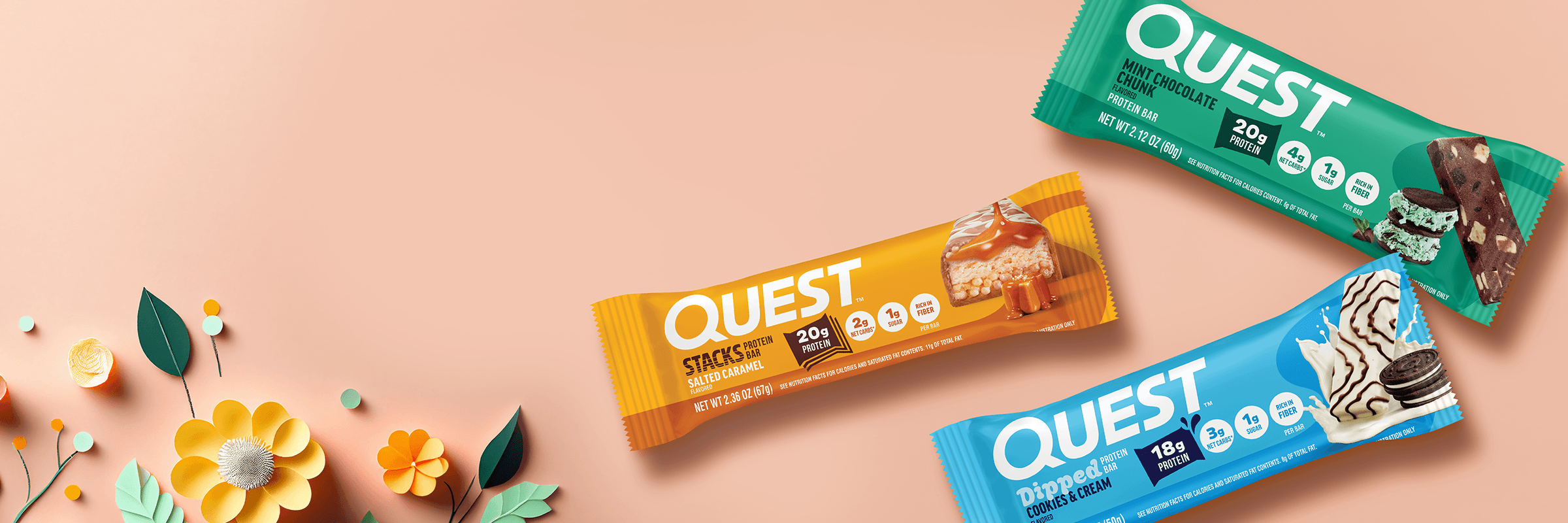 Three Quest protein bars are arranged on a peach background. The bars, in orange, turquoise, and green packaging, are surrounded by paper-cut art flowers on the left, creating a cheerful and vibrant scene.
