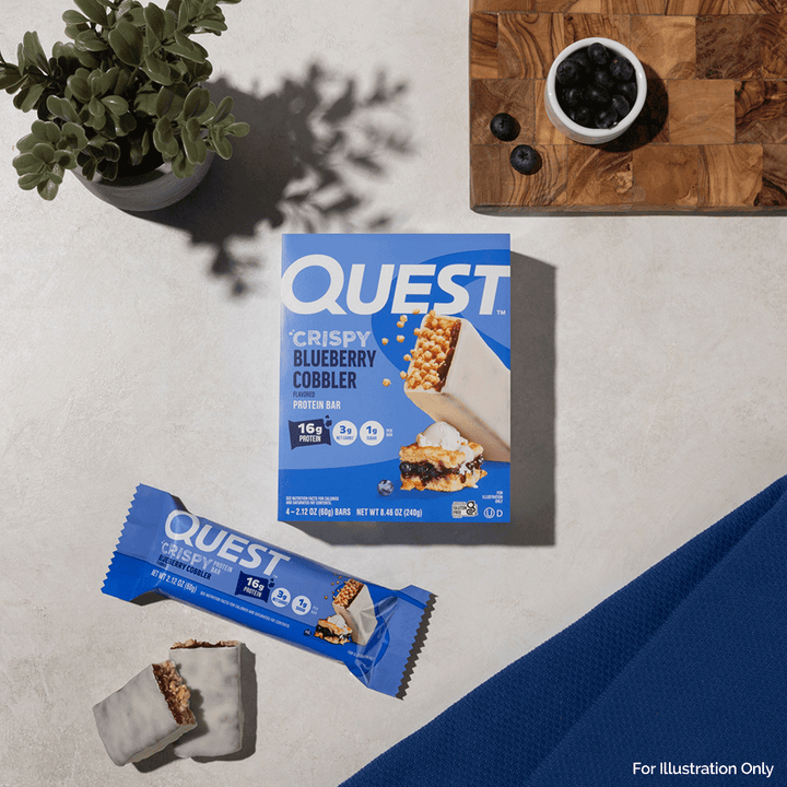 Quest Crispy Blueberry Cobbler protein bar packaging on a light surface with a plant and cutting board in the background.