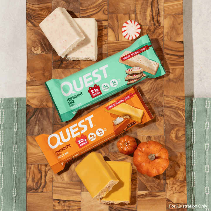 Two Quest snack bars, one peppermint milk chocolate and one pumpkin pie cheese with cream cheese, arranged on a wooden board with candy canes, small pumpkins, and cheese slices.