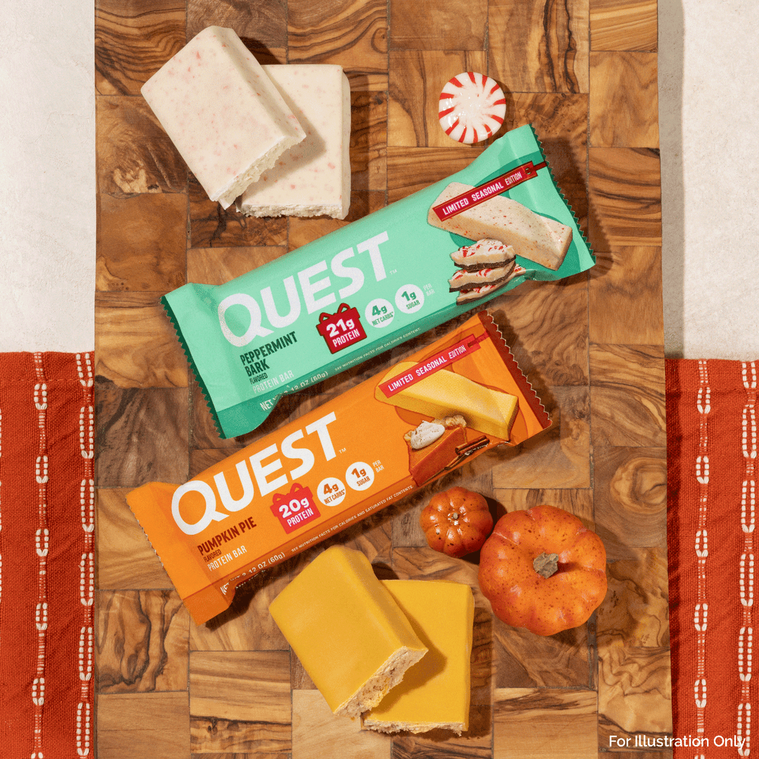 Two Quest snack bars, one Peppermint Milk Chocolate and one Pumpkin Pie Chocolate, arranged on a wooden board with candy canes, small pumpkins, and cheese slices. The Quest packaging is visible, and the scene is styled with autumn-themed props.