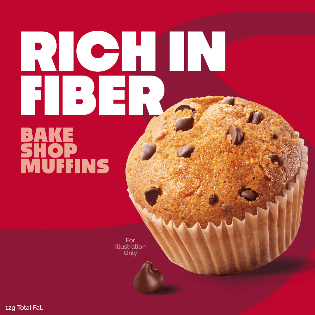 A promotional graphic for chocolate chip muffins on a red background. Large white text reads 'RICH IN FIBER' and smaller pink text reads 'BAKE SHOP MUFFINS.