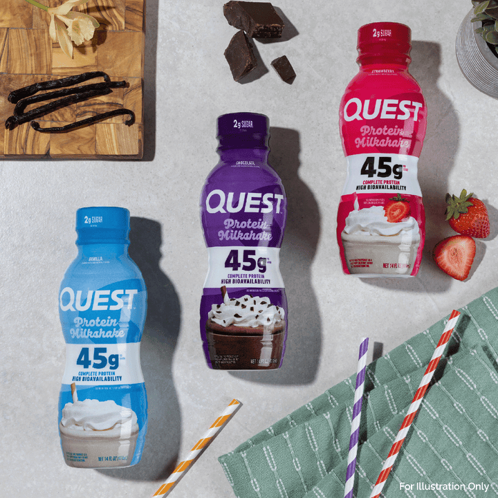 Three Quest Protein Milkshake bottles in blue, purple, and red flavors arranged on a light gray surface with food props including chocolate pieces, vanilla beans, strawberries, and striped straws.